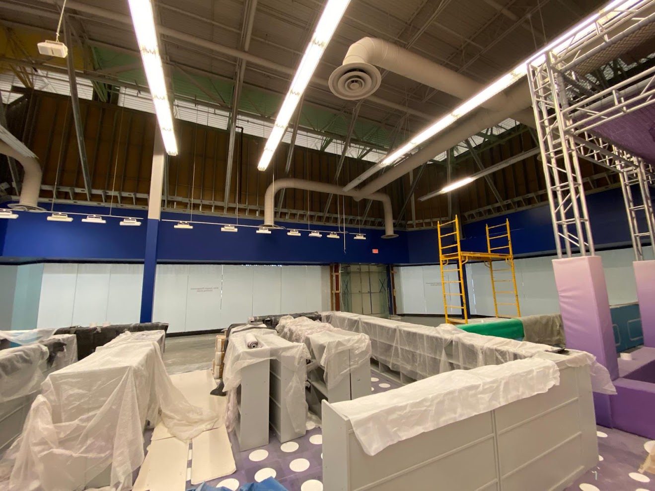 Professional painting preparation in gymnasium with extensive masking and equipment protection