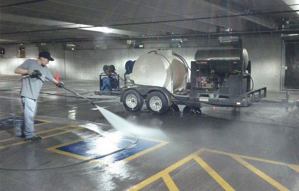 Professional power washing technician cleaning parking garage with truck-mounted equipment